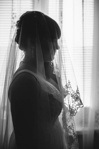 Young beautiful bride waits for groom near the window. Beautiful  young woman standing beside a large window waiting — Stock Photo, Image