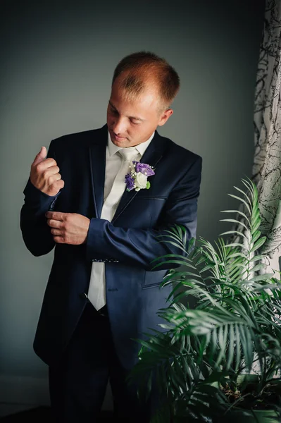 Portret van knappe bruidegom in klassiek interieur. Mens tegen venster achtergrond jurk Manchetknopen. — Stockfoto