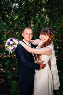 evlilik çift yeşil yaz parkta öpüşme. Gelin ve damat öpüşme, birlikte açık havada duran, yeşil ağaçlar arasında sarılma. Gelin düğün buket çiçek tutan