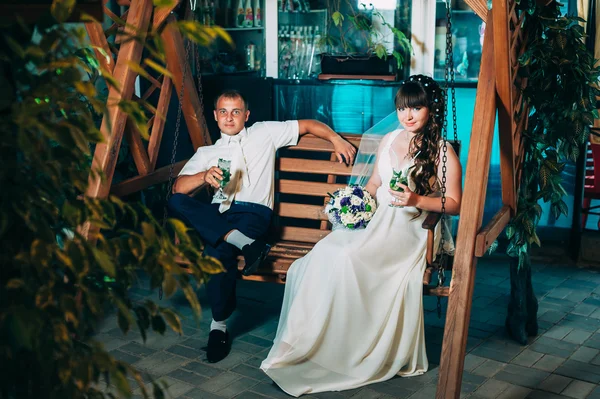 Glückliche Braut und Bräutigam trinken Mojito, schwingen auf einer Schaukel — Stockfoto