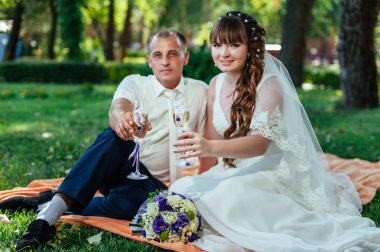 Yeni evli çift park yeşil çim buket çiçek ve şarap bardakları ile oturuyor