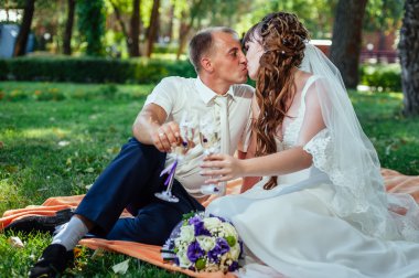 Yeni evli çift park yeşil çim buket çiçek ve şarap bardakları ile oturuyor