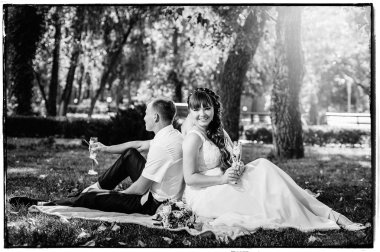 Yeni evli çift park yeşil çim buket çiçek ve şarap bardakları ile oturuyor