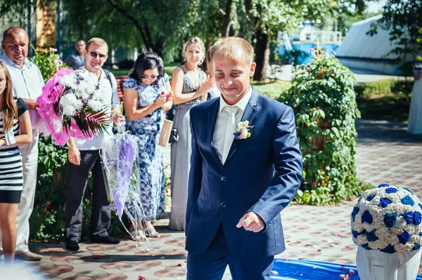 Csodálatos elegáns gazdag boldog vőlegény az esküvő, a zöld kert közelében a virágok fehér arch — Stock Fotó