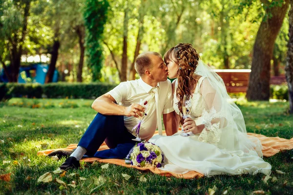 Paar, das gerade geheiratet hat, sitzt im grünen Gras des Parks mit Blumenstrauß und Weingläsern — Stockfoto