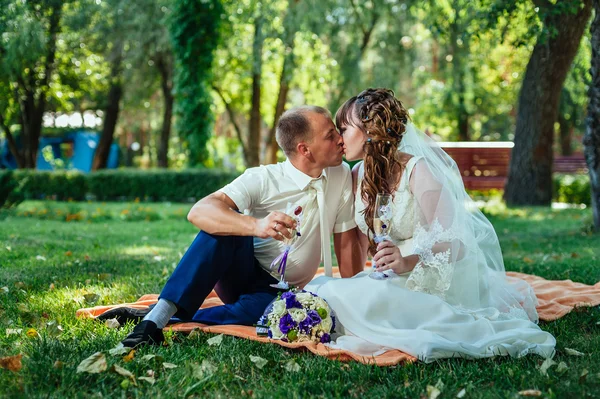 Csak házasok ül park zöld fű, csokor virágot és borospohár — Stock Fotó
