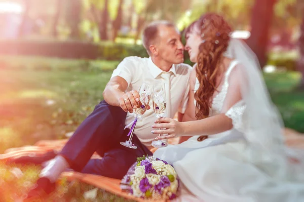 Пара только что вышла замуж сидя в парке зеленой травы с букетом цветов и бокалов вина — стоковое фото