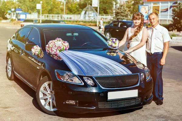 Beautiful brunette bride at white wedding with her handsome young groom in black suit stand near the car — Stock Photo, Image