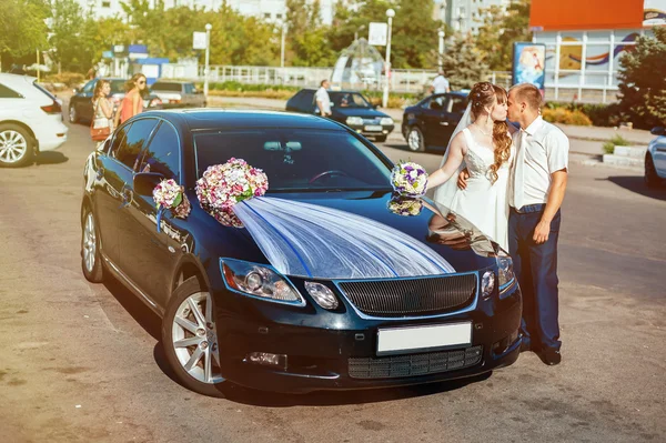 Beautiful brunette bride at white wedding with her handsome young groom in black suit stand near the car — Stock Photo, Image