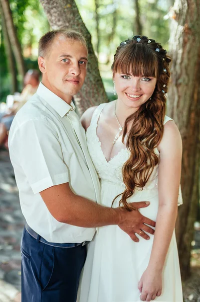 Wedding couple kissing in green summer park. bride and groom kissing, standing together outdoors, hugging among green trees. Bride holding wedding bouquet of flowers — Stock Photo, Image