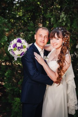 evlilik çift yeşil yaz parkta öpüşme. Gelin ve damat öpüşme, birlikte açık havada duran, yeşil ağaçlar arasında sarılma. Gelin düğün buket çiçek tutan