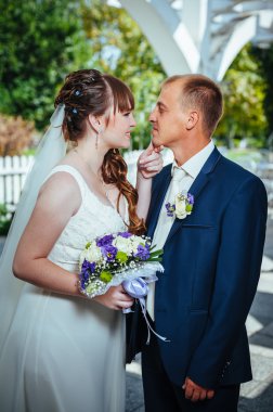 evlilik çift yeşil yaz parkta öpüşme. Gelin ve damat öpüşme, birlikte açık havada duran, yeşil ağaçlar arasında sarılma. Gelin düğün buket çiçek tutan