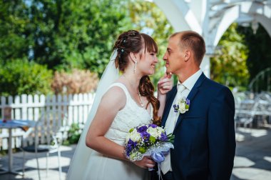 evlilik çift yeşil yaz parkta öpüşme. Gelin ve damat öpüşme, birlikte açık havada duran, yeşil ağaçlar arasında sarılma. Gelin düğün buket çiçek tutan