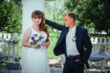 evlilik çift yeşil yaz parkta öpüşme. Gelin ve damat öpüşme, birlikte açık havada duran, yeşil ağaçlar arasında sarılma. Gelin düğün buket çiçek tutan