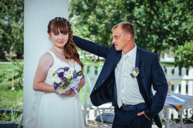 evlilik çift yeşil yaz parkta öpüşme. Gelin ve damat öpüşme, birlikte açık havada duran, yeşil ağaçlar arasında sarılma. Gelin düğün buket çiçek tutan