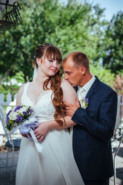 evlilik çift yeşil yaz parkta öpüşme. Gelin ve damat öpüşme, birlikte açık havada duran, yeşil ağaçlar arasında sarılma. Gelin düğün buket çiçek tutan