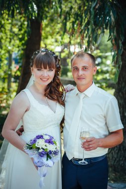 evlilik çift yeşil yaz parkta öpüşme. Gelin ve damat öpüşme, birlikte açık havada duran, yeşil ağaçlar arasında sarılma. Gelin düğün buket çiçek tutan