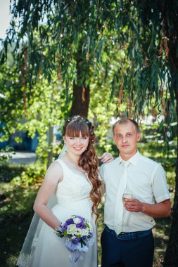 evlilik çift yeşil yaz parkta öpüşme. Gelin ve damat öpüşme, birlikte açık havada duran, yeşil ağaçlar arasında sarılma. Gelin düğün buket çiçek tutan