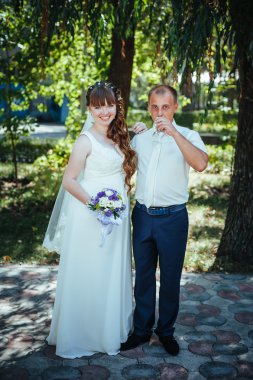 evlilik çift yeşil yaz parkta öpüşme. Gelin ve damat öpüşme, birlikte açık havada duran, yeşil ağaçlar arasında sarılma. Gelin düğün buket çiçek tutan