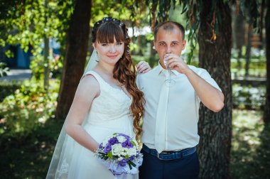 evlilik çift yeşil yaz parkta öpüşme. Gelin ve damat öpüşme, birlikte açık havada duran, yeşil ağaçlar arasında sarılma. Gelin düğün buket çiçek tutan