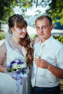 evlilik çift yeşil yaz parkta öpüşme. Gelin ve damat öpüşme, birlikte açık havada duran, yeşil ağaçlar arasında sarılma. Gelin düğün buket çiçek tutan