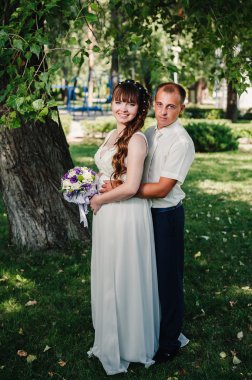 evlilik çift yeşil yaz parkta öpüşme. Gelin ve damat öpüşme, birlikte açık havada duran, yeşil ağaçlar arasında sarılma. Gelin düğün buket çiçek tutan