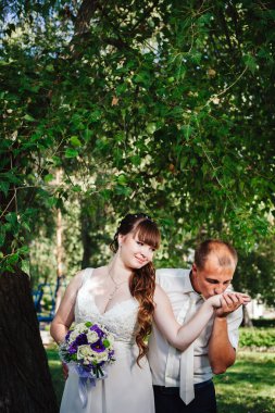 evlilik çift yeşil yaz parkta öpüşme. Gelin ve damat öpüşme, birlikte açık havada duran, yeşil ağaçlar arasında sarılma. Gelin düğün buket çiçek tutan