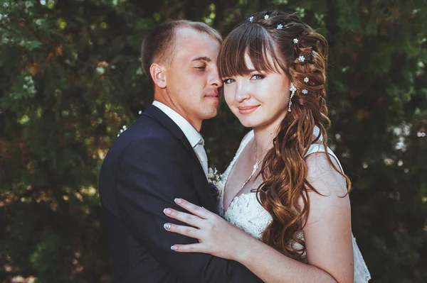 Couple de mariage embrasser dans le parc vert d'été. baiser de mariée et marié, debout ensemble à l'extérieur, étreignant parmi les arbres verts. Mariée tenant bouquet de mariage de fleurs — Photo