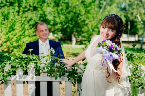 Para ślub całowanie w lato zielony park. panny młodej i pana młodego, całowanie, stojąc razem na zewnątrz, przytulanie wśród zieleni drzew. Panna młoda trzyma Bukiet ślubny, kwiaty — Zdjęcie stockowe