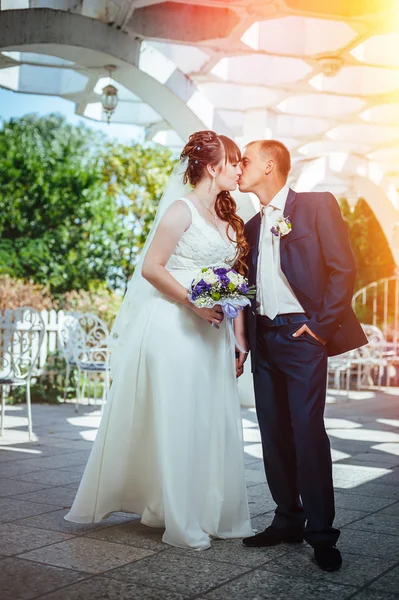 Pareja de boda besándose en verde parque de verano. novia y novio besándose, de pie juntos al aire libre, abrazándose entre árboles verdes. Novia celebración de la boda ramo de flores —  Fotos de Stock