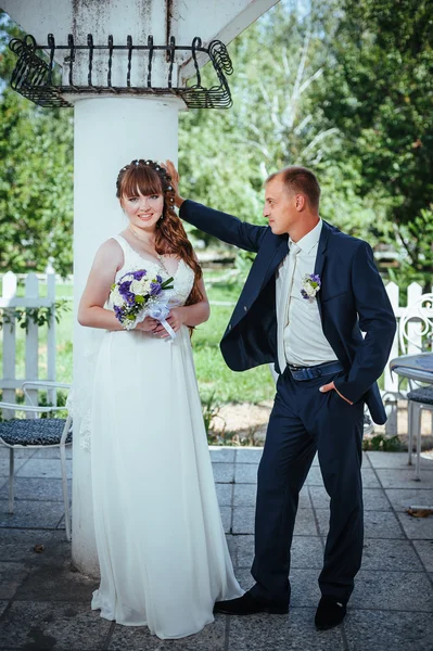 Casamento casal beijando no parque de verão verde. noiva e noivo beijando, de pé juntos ao ar livre, abraçando entre árvores verdes. Noiva segurando buquê de casamento de flores — Fotografia de Stock