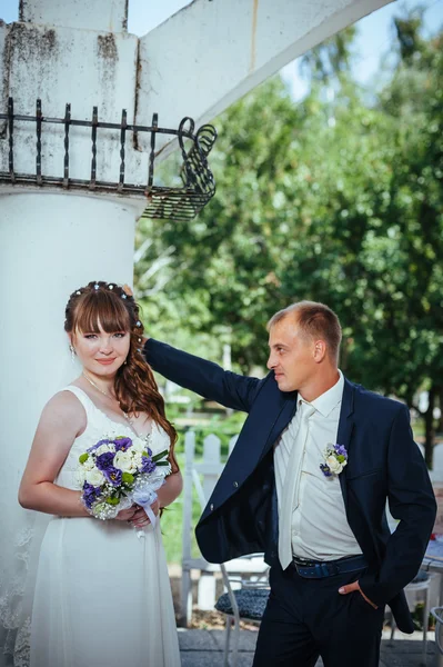 Wedding couple kissing in green summer park. bride and groom kissing, standing together outdoors, hugging among green trees. Bride holding wedding bouquet of flowers — Stock Photo, Image