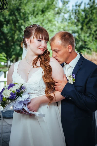 Matrimonio coppia baciarsi nel verde parco estivo. sposa e sposo baciarsi, stare insieme all'aperto, abbracciarsi tra alberi verdi. Sposa tenuta bouquet da sposa di fiori — Foto Stock