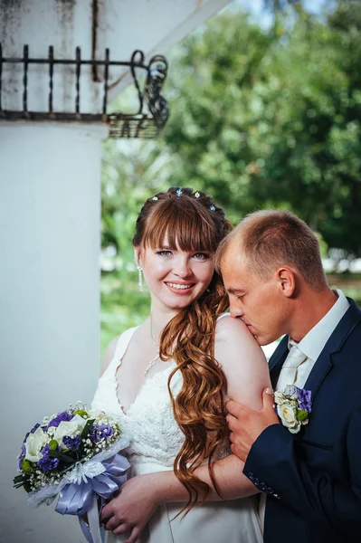 Γαμήλιο ζεύγος φιλιά στο πάρκο πράσινο το καλοκαίρι. νύφη και ο γαμπρός φιλιά, στέκεται έξω μαζί, το αγκάλιασμα μεταξύ πράσινα δέντρα. Νύφη κρατώντας γαμήλιας ανθοδέσμης των λουλουδιών — Φωτογραφία Αρχείου