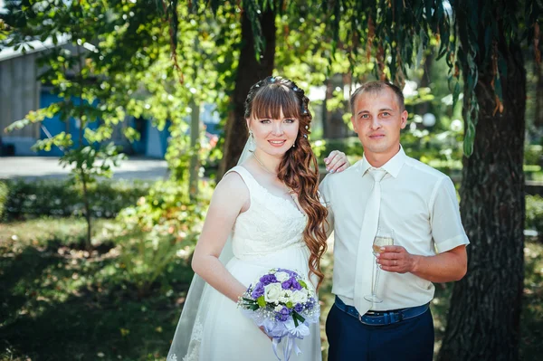 Brudparet kyssas i gröna sommaren park. Brudparet kysser, ständiga tillsammans utomhus, kramas bland gröna träd. Brud holding bröllop bukett blommor — Stockfoto