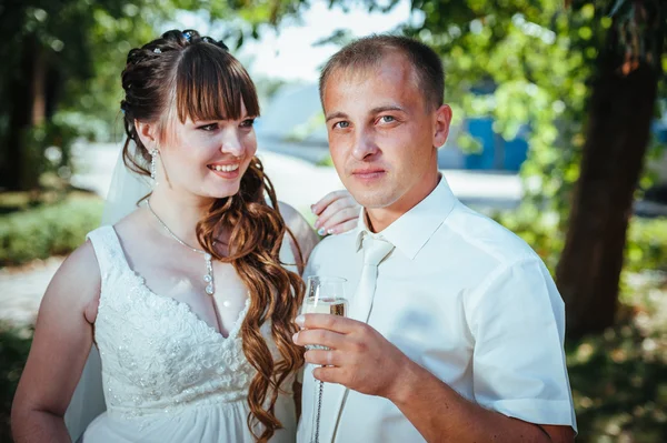 Brudparet kyssas i gröna sommaren park. Brudparet kysser, ständiga tillsammans utomhus, kramas bland gröna träd. Brud holding bröllop bukett blommor — Stockfoto