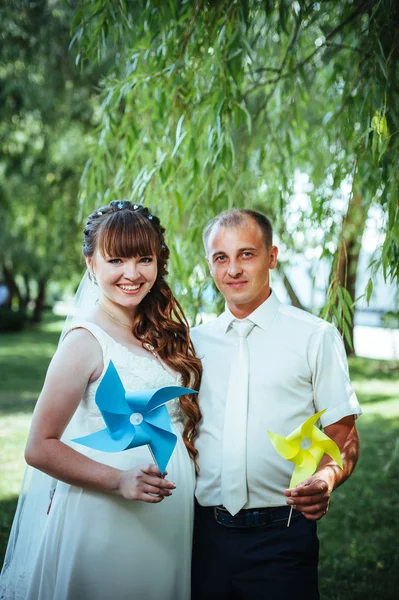 Wedding couple kissing in green summer park. bride and groom kissing, standing together outdoors, hugging among green trees. Bride holding wedding bouquet of flowers — Stock Photo, Image