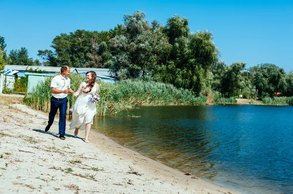 Een bruiloft door de zee. Huwelijksreis. De bruid en bruidegom knuffelen op de oever van het meer. bruid en bruidegom knuffelen op een groen meer. Bruid en bruidegom in een park. trouwjurk. Bruids bruiloft boeket van bloemen — Stockfoto