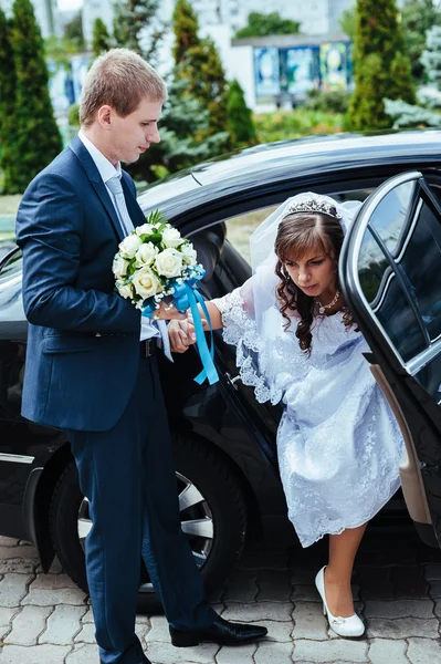 Happy groom helping his bride out of the wedding car. — Stock Photo, Image