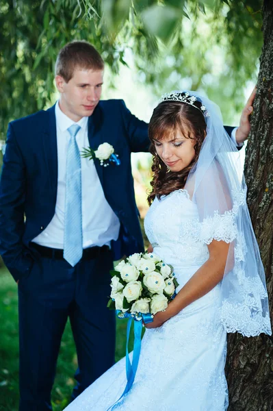 Novia y novio en el día de la boda caminando al aire libre en la naturaleza de primavera. Pareja nupcial, feliz pareja recién casada abrazándose en el parque verde . — Foto de Stock