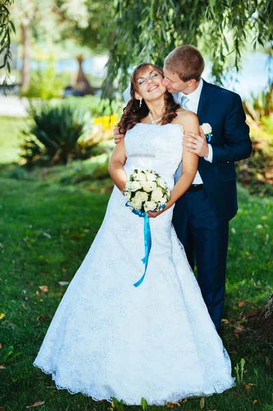 Novia y novio en el día de la boda caminando al aire libre en la naturaleza de primavera. Pareja nupcial, feliz pareja recién casada abrazándose en el parque verde . — Foto de Stock