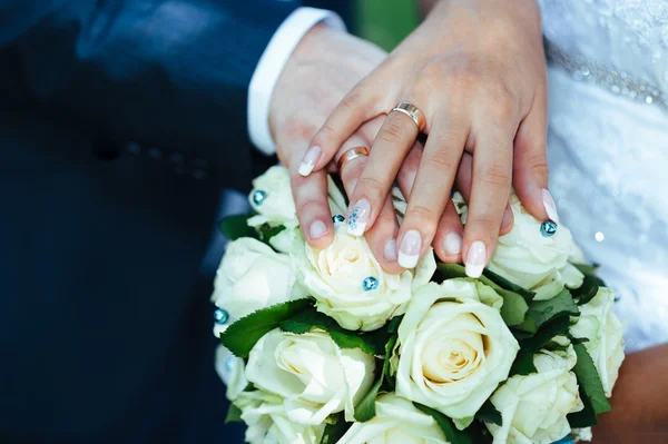 Руки жениха и невесты с кольцами на красивом свадебном букете — стоковое фото