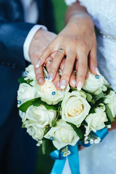 Руки жениха и невесты с кольцами на красивом свадебном букете — стоковое фото