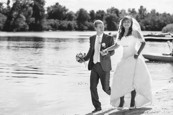 Loving wedding couple standing and kissing near water — Stock Photo, Image