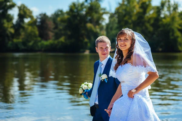 Loving wedding couple standing and kissing near water — Stock Photo, Image