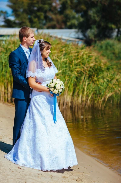 Milující Svatební pár stojící a líbání u vody — Stock fotografie