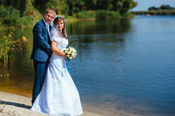 Loving wedding couple standing and kissing near water — Stock Photo, Image