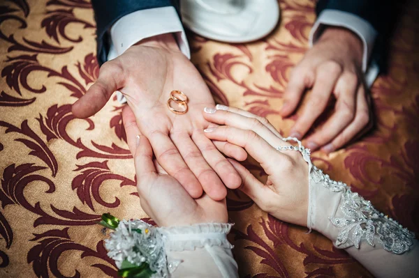 Casais de casamento mãos sobre a mesa e anéis, flores do buquê de noiva — Fotografia de Stock