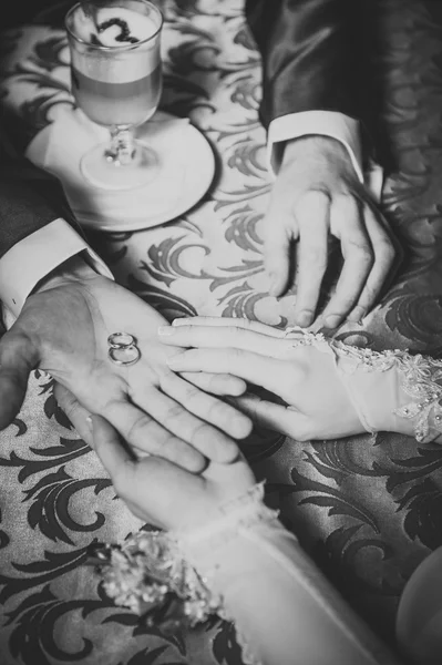 Casais de casamento mãos sobre a mesa e anéis, flores do buquê de noiva — Fotografia de Stock