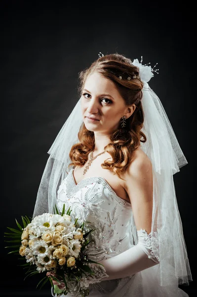 Modèle de mode avec bouquet nuptial buvant du champagne et portant une robe de mariée à fond noir studio — Photo